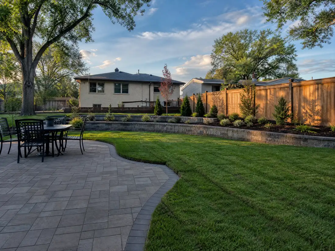 A completed landscaping project in a Saskatoon, SK back yard with a paving stone patio, new sod lawn and a block retaining wall